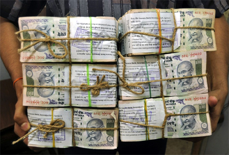 A banker carries stacks of rupee notes.