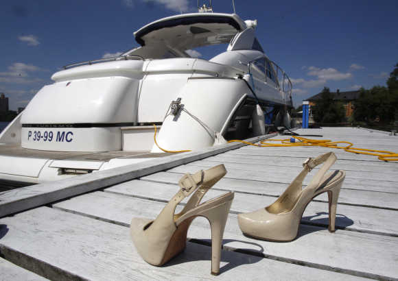 A pair of high heel shoes is placed on shore in front of a yacht.
