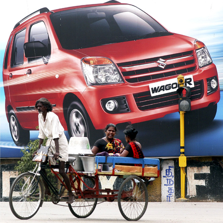 A rickshaw-puller peddles in front of a billboard for the WagonR, a car manufactured by Maruti Suzuki.