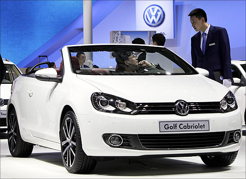 A visitor sitting in a Volkswagen Golf Cabriolet speaks to a staff member at Auto China 2012 in Beijing.