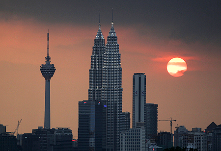 The sun sets near the Petronas Twin Towers and Kuala Lumpur Tower (left).