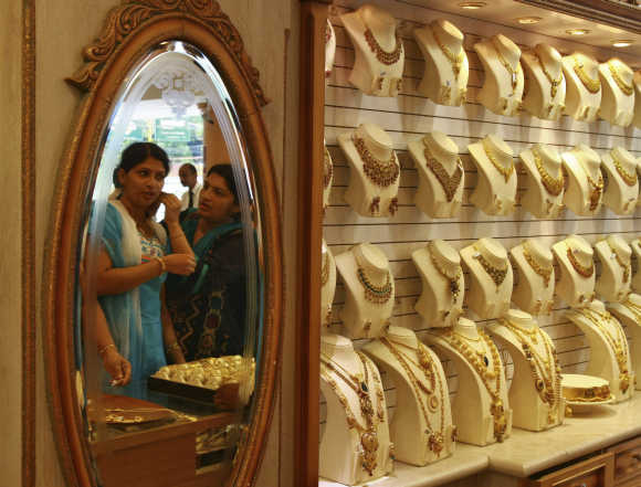 A woman is reflected in a mirror as she tries a gold earring inside a jewellery showroom in Kochi.