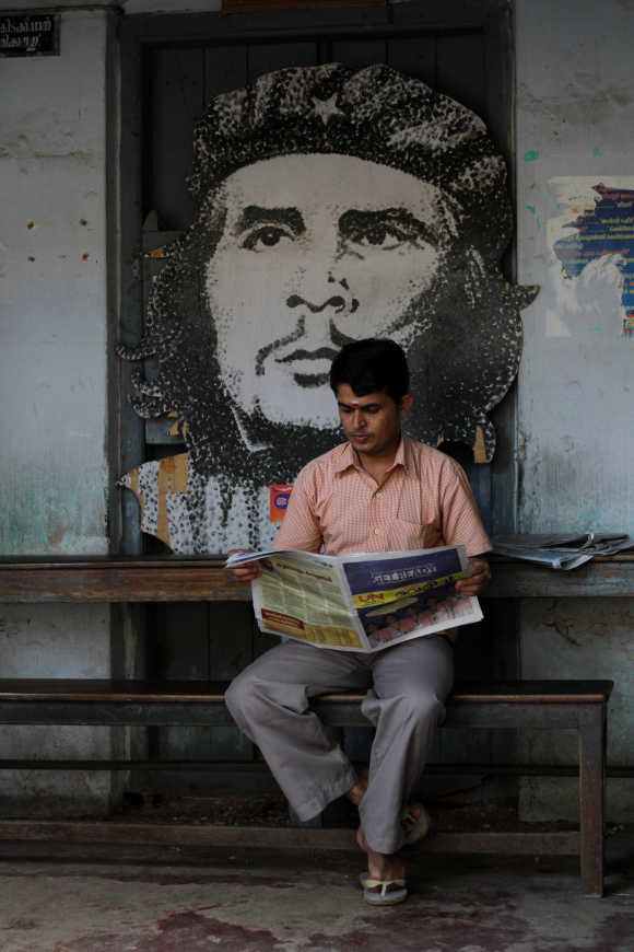 A man reads a newspaper in front of a cardboard cutout of Ernesto Che Guevara in Kerala.