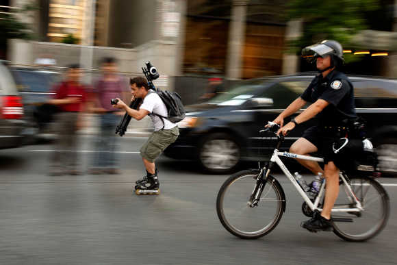 A man on rollerblades carrying cameras rolls along with bicycle police in Toronto.