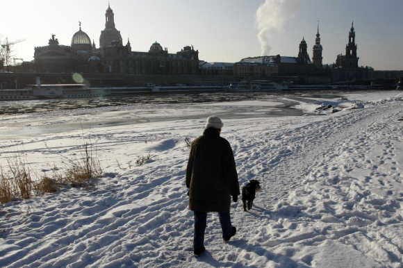 A women and her dog walks along the frozen river bank in front of the old city at river Elbe in Dresden