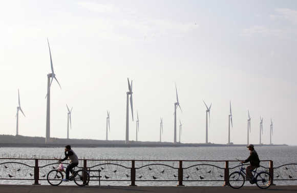 People ride their bicycles in front of wind turbines that generate electricity in Gaomei Wetland in Taichung, Taiwan.