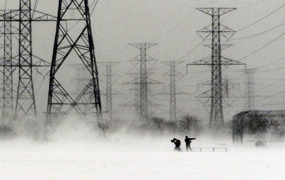 Students, walking to school, are dwarfed by power towers as they fight their way across an open field, during a winter storm, in Pickering east of Toronto.