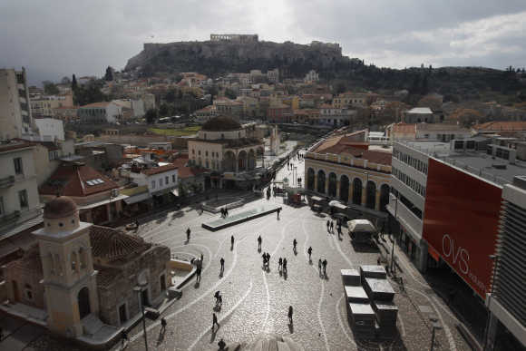 People walk on the Monastiraki square as the Acropolis hill is seen in the background in central Athens.