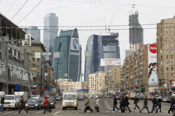 People cross a road, with the Vostok or East tower, seen in the background in Moscow.