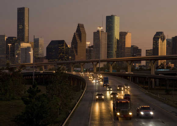 Traffic flows at dusk with the downtown Houston skyline in the background as night falls.