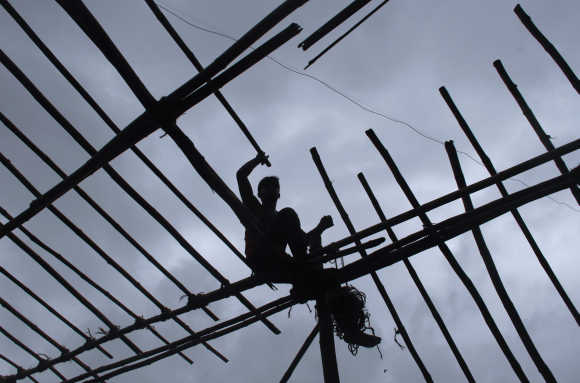 A man is silhouetted against the sky while sitting on wooden scaffolding, as he constructs a temporary tent in Mumbai.