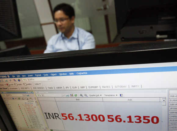 A foreign exchange trader works as the exchange rate of the Indian rupee to US dollar is displayed on a screen at a trading firm in Mumbai.