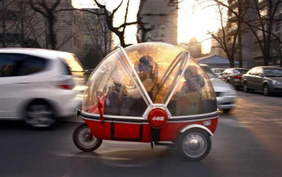 A woman and her son sit inside the capsule of an electric tricycle as they drive along a main road in central Beijing.