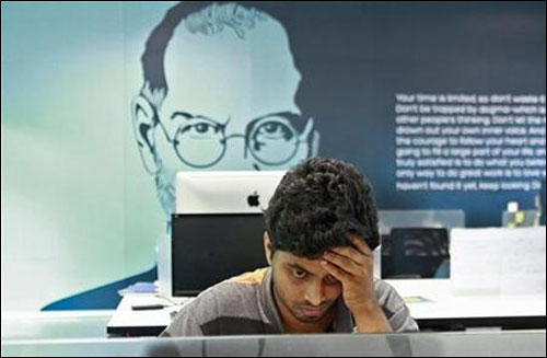 An employee works on a computer terminal against the backdrop of a picture of late Apple co-founder Steve Jobs at the Start-up Village.