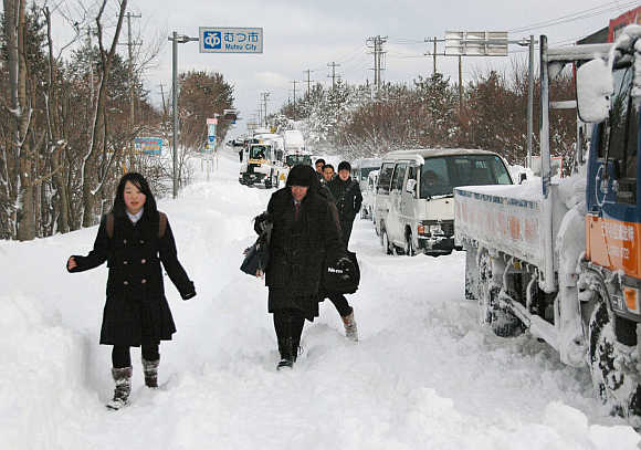 People walk past vehicles stranded in heavy snow near Niigata.