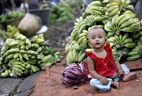 A toddler sits infront of piles of bananas at a shop in a market in Yangon.