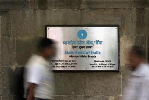 People walk in front of a signboard displayed at the head office of State Bank of India in Mumbai