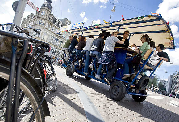 Tourists cycle as they drink beer and sing karaoke on a beerbike in Amsterdam.