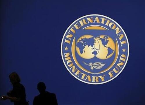 Visitors are silhouetted against the logo of the International Monetary Fund.