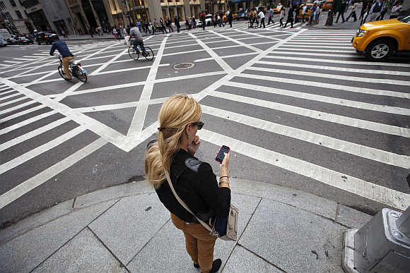 A woman uses Apple iPhone while waiting to cross Fifth Avenue in New York.