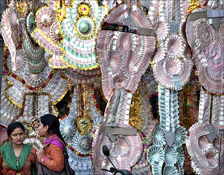 Women stand next to a shop selling garlands made of Indian currency notes.