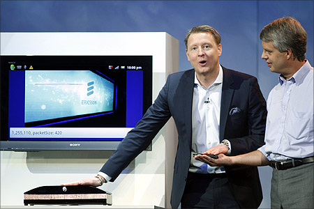 Hans Vestberg (L), president and chief executive of the Ericsson Group, transfers a photo from a smartphone to a computer screen using his body.