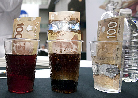 New Canadian 100 dollar bills made of polymer are placed in  glasses of juice, cola and water in Toronto.