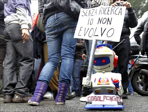 A small toy robot holds up a sign which reads, without research I can't evolve, during a demonstration in Rome.