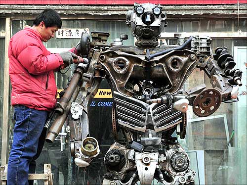 Huang Lianfei, a worker at a metal craft workshop, stands on a ladder as he drills to construct a model robot based on a character from the cartoon Transformers.