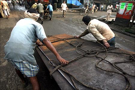 Workers pull a cart laden with metal sheets at an industrial area in Mumbai.