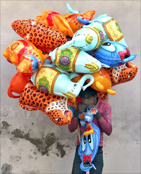 A vendor blows a toy balloon for sale on a street at Noida on the outskirts of New Delhi.