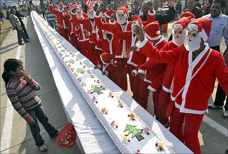 People dressed in Santa Claus costumes dance before they cut a 101-feet (31-metres) long cake as part of Christmas celebrations.