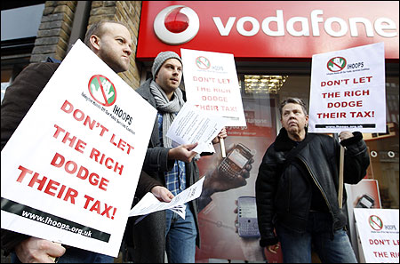 Demonstrators stand poutside a branch of Vodafone as they protest against the company not paying enough tax.