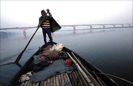 A man rows his boat in the waters of river Ganges with Mahatma Gandhi Setu bridge.