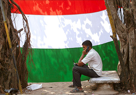 man speaks on the phone outside his shanty in front of an Indian national flag in Dharavi.