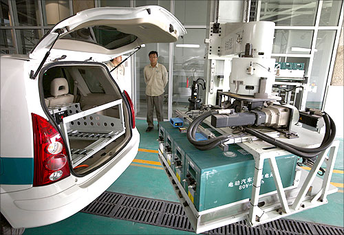 Workers watch as a battery exchange robot changes the batteries in an electric car at China's largest electric vehicle battery recharging station in Beijing.
