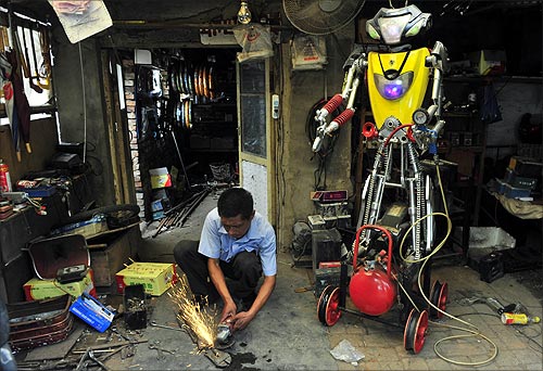 A 49-year-old electric bike mechanic who identified himself only as Wu welds a component to fit onto his newly-made robot (R) at his repair shop in Shenyang, Liaoning province.
