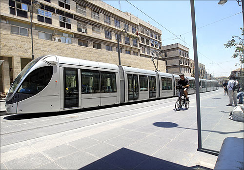 A man rides a bicycle next to a light rail tram in Jerusalem.