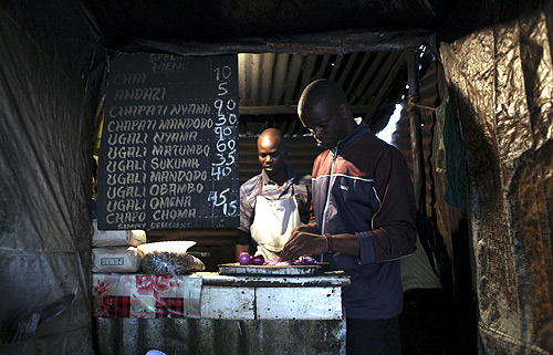Denis Onyango Olang, (R), a 26 year-old assistant cook, prepares food in a dimly lit kitchen at a hotel in Nairobi's Kibera slum in the Kenyan capital.