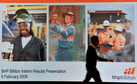 Man walks past screen displaying images for BHP Billiton interim results briefing in London.