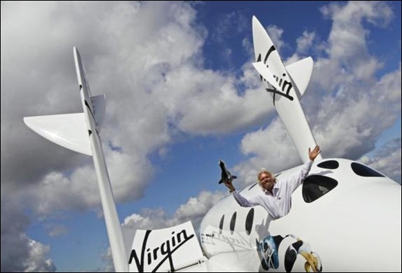 Entrepreneur Branson waves a model of LauncherOne cargo spacecraft from a window of an actual size model of SpaceShipTwo.