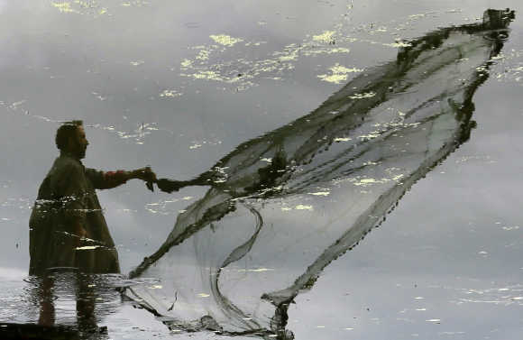 A Kashmiri fisherman is reflected in the waters of Dal Lake as he throws a net to catch fish in Srinagar.