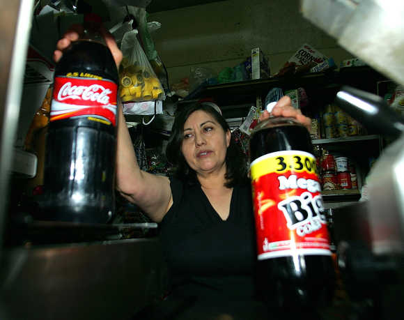 Raquel Chavez, 49, owner of the La Racha's store shows a Coca-Cola bottle and a Big Cola bottle in Mexico City.