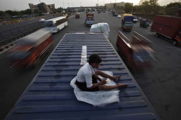 Helper of a driver rests on top of his parked truck along a busy highway on the outskirts of New Delhi.