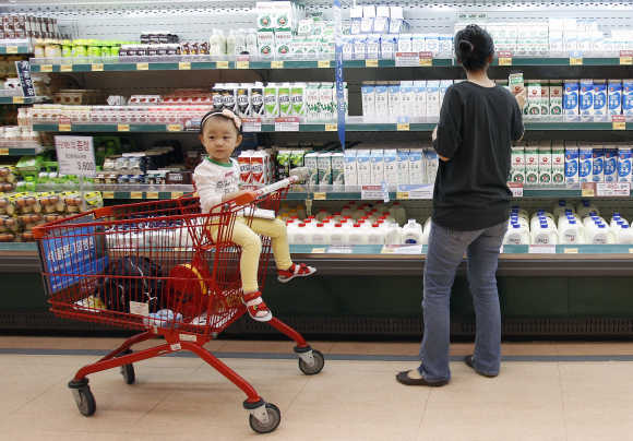 A customer looks at milk as a girl sits on a shopping cart at a supermarket in Seoul.