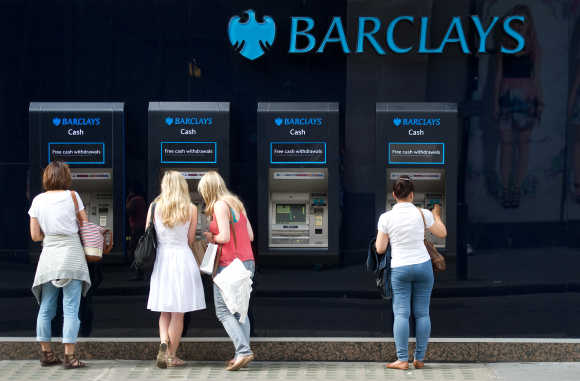 People use a line of Barclays cash dispensers in central London.