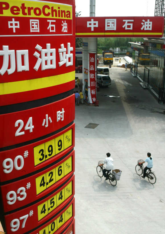 Cyclists pass under board displaying oil prices at PetroChina station in Beijing.