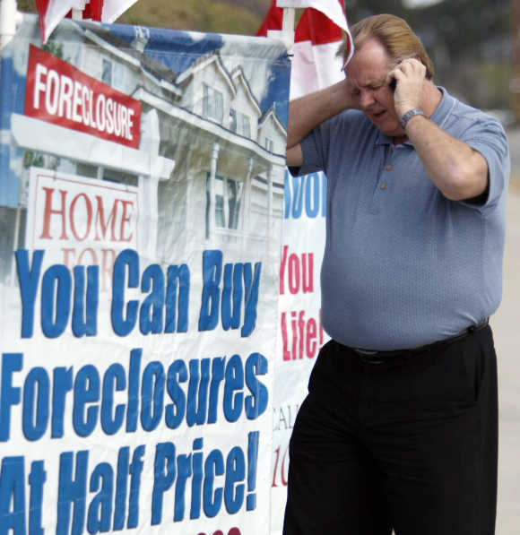 Home Center Realty owner Ron Barnard talks on his mobile phone as he stands next to a sign advertising his business in Norco, California.