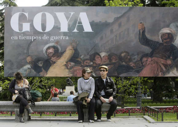 People sit in front of a banner announcing Goya exhibition in Madrid.