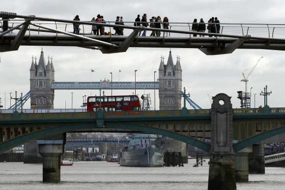 Pedestrians cross the Millenium Bridge spanning the Thames River in London.